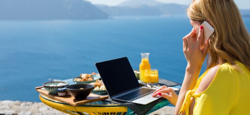 A woman working on a laptop while travelling overseas and discussing remortgaging a UK buy-to-let from overseas by phone.
